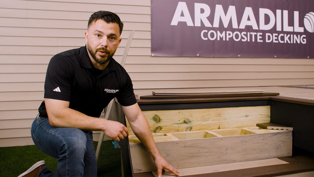Derek kneeling by steps pointing to contrasting boards on composite deck staircase