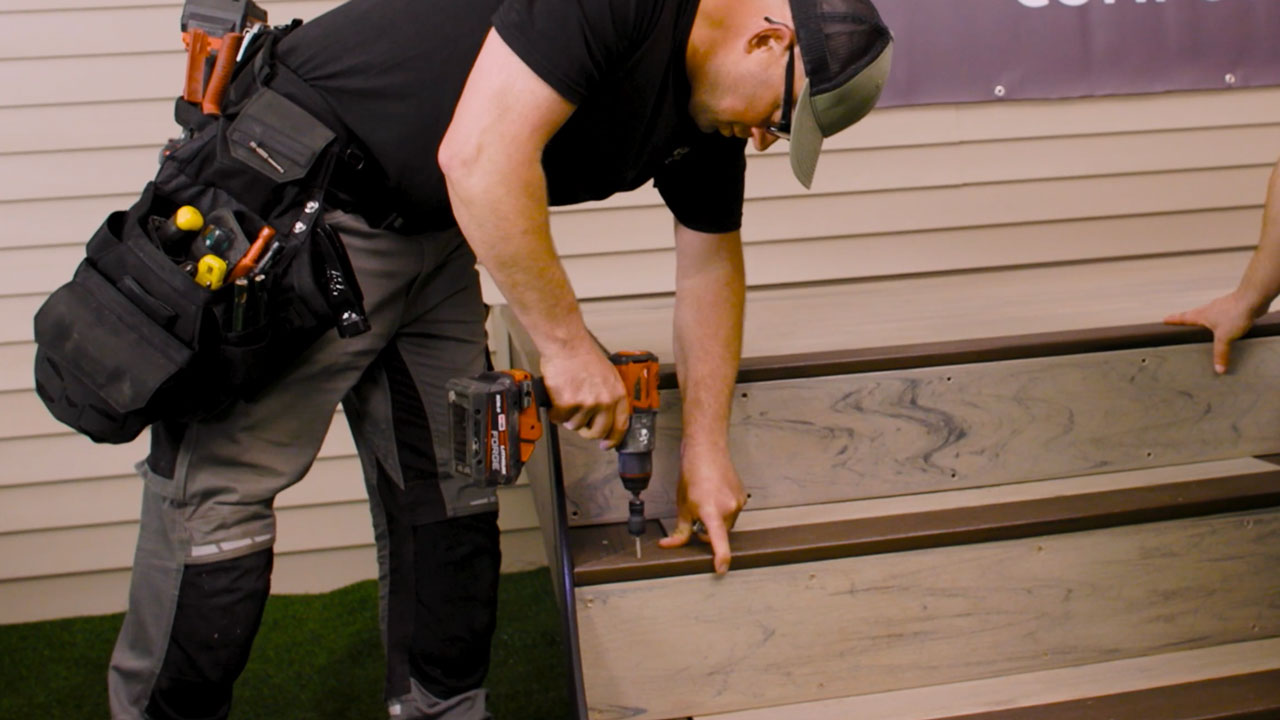 Contractor screwing down boards to complete composite deck staircase with picture frame design